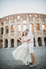 young beautiful couple in white clothes stands against the background of the Colosseum in Rome in Italy