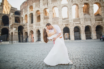 young beautiful couple in white clothes stands against the background of the Colosseum in Rome in Italy