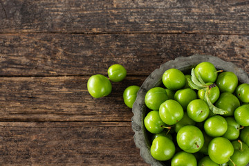 Many isolated green sour plums in a bowl on the rustic wooden table