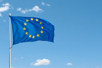 European Union flag on flag pole waving in the air on blue sky background. Copy space