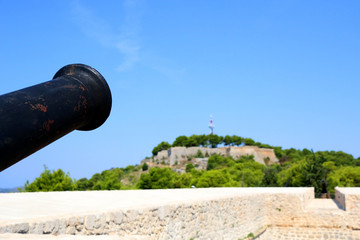 Fototapeta na wymiar Historic cannon on Barone Fortress in Sibenik, Croatia. View of St. John Fortress in the background.