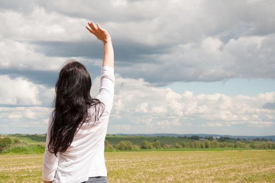 A woman with her hands up on a green field praises God. Prayer with arms raised. Blue sky and white clouds....