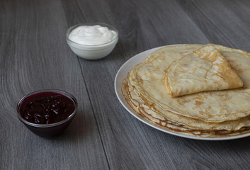Stack of thin pancakes with jam and sour cream