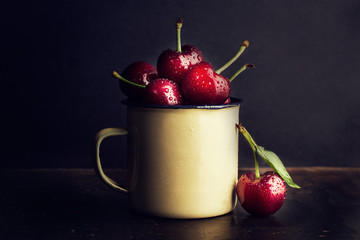 Cerezas dentro de una taza antigua sobre fondo negro vista de frente