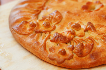 Russian pie with potatoes and mushrooms on the table. Freshly baked big cake decorated with flowers of their dough
