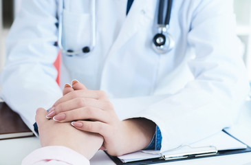 Friendly female doctor hands holding patient hand sitting at the desk for encouragement, empathy, cheering and support while medical examination. Just hands over the table.