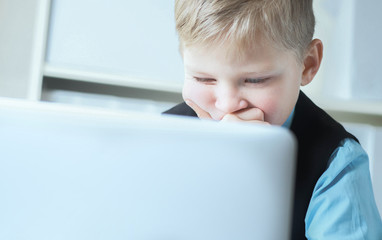 Small cute boy in business suit with a tie works at computer at office. Small business man, little boss.