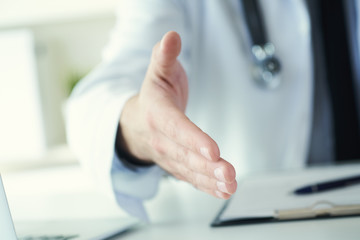 Male medicine doctor offering hand to shake in office closeup. Greeting and welcoming gesture. Medical cure and tests advertisement concept.