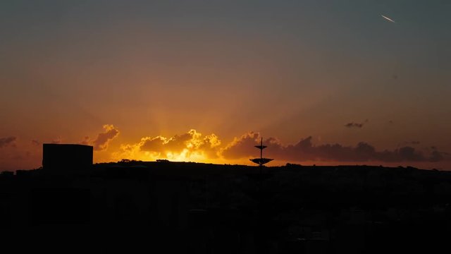 Time Lapse video showing golden hour of sunset with backlit clouds and dark silhouette of foreground below. Shot at the island of Gozo in Malta in the Mediterranean.