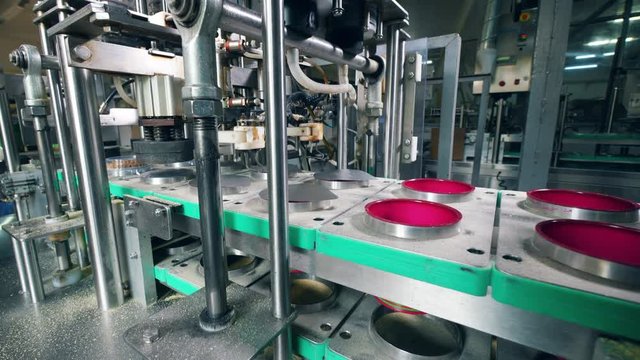 Factory machines placing caps on plastic container on a conveyor.