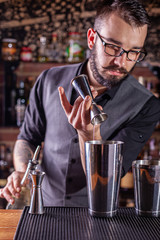 barman preparing cocktai and pours liquid into the jigger in a cocktail bar