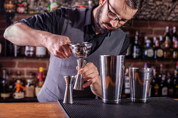 barman in bar interior squeezes lime juice into a chilled shaker. Portrait of a professional bartender at work in night club with squeezer in hands. Service industry occupation.