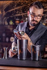 barman preparing cocktai and pours liquid into the jigger in a cocktail bar