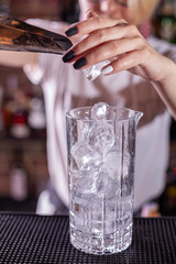 Barman puts the ice cubes into a glass with a red cocktail