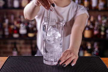 Professional bartender girl stiring a delicious red cocktail in the glass at the steel bar counter