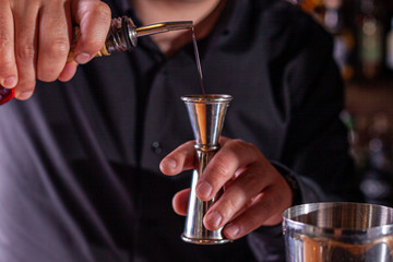 barman preparing cocktai and pours liquid into the jigger in a cocktail bar