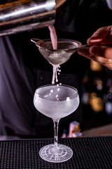 Bartender pouring a cocktail from the steel shaker on the bar counter on the blurred background