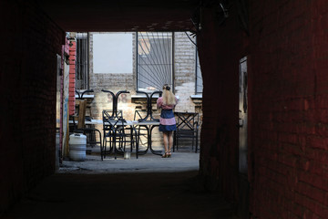 The passage to the old courtyard in the ancient city illuminated by the sun. Table, chairs and a girl with a phone