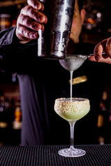 Bartender pouring a cocktail from the steel shaker on the bar counter on the blurred background