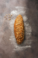 A loaf of fresh bread with sunflower seeds, sesame on a dark rustic background. Top view, copy space.