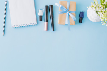 Flat lay blogger or freelancer workspace with a notebook, gift box and lily of the valley flowers on a blue background