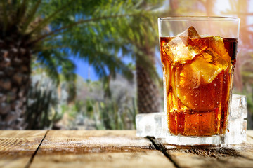 Fresh cold ice tea on desk and blurred background of palms. 