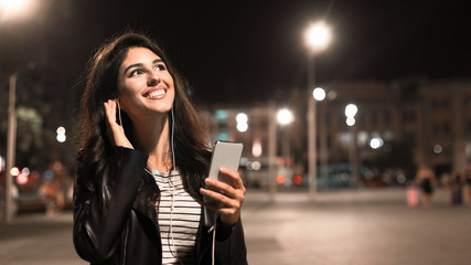 Calm evening. Girl listening music in earphones in the city