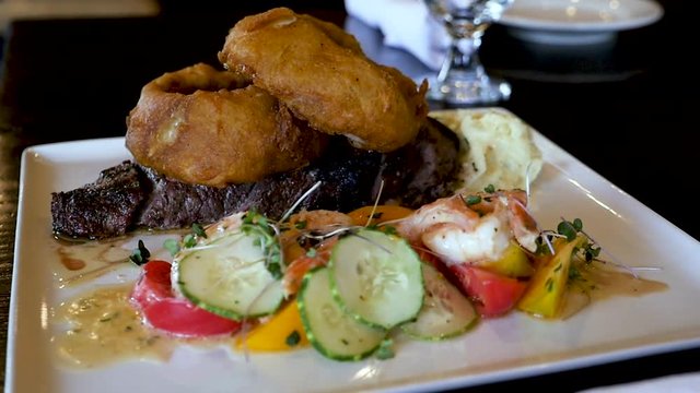 chefs special steak shrimp oinion rings in restaurant. This quick clip is of a plated steak with large onion rings on top of it with vegetables on the side.