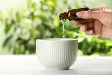 Woman pouring essential oil from bottle into bowl on table