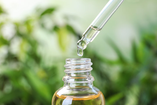 Dropping essential oil into glass bottle on blurred background, closeup