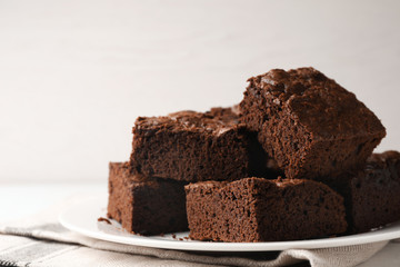 Plate with fresh brownies on white table against light background, space for text. Delicious...