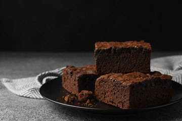 Plate with fresh brownies on grey table against black background, space for text. Delicious...