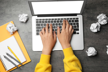 Woman using laptop at table with crumpled paper, top view. Generating idea