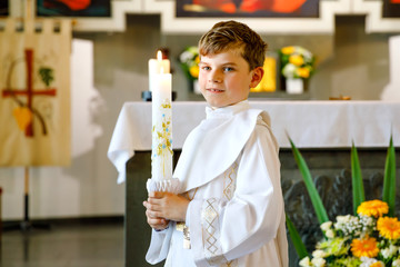 Little kid boy receiving his first holy communion. Happy child holding Christening candle....