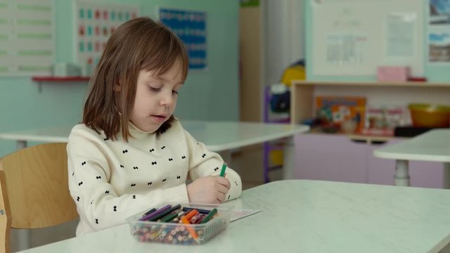 Girl preschooler in kindergarten. The girl draws with pencils. Blurred background.