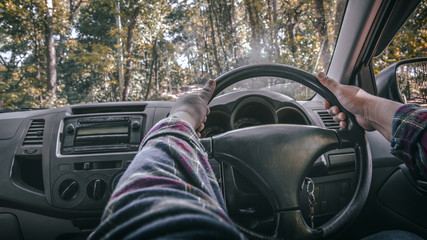Close up hands holding steering wheel driving in the forest road.