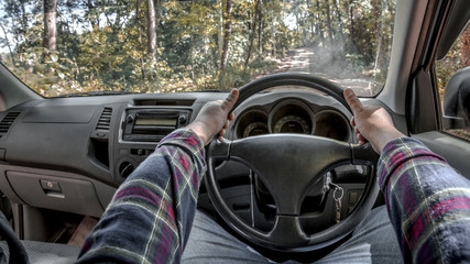 Close up two hands holding steering wheel driving in the forest road.