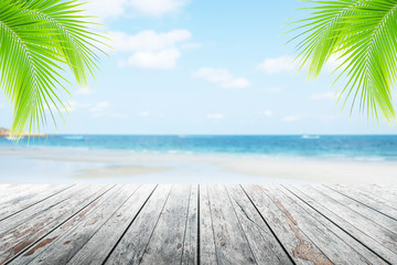 Empty wooden table or dock floor and palm leaves with blurred background, beach and beautiful sea in daytime.
