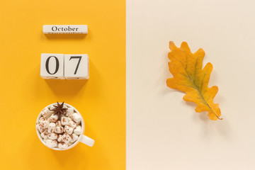 Autumn composition. Wooden calendar October 7, cup of cocoa with marshmallows and yellow autumn...