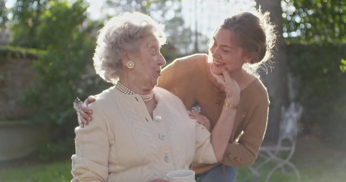 Granddaughter visiting,happy hugging grandmother at outside garden,backlight sun. Multigeneration women love holding together.White hair elderly grandma woman.Affection,togetherness,caring,loving