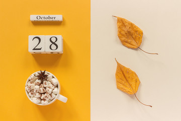 Autumn composition. Wooden calendar October 28, cup of cocoa with marshmallows and yellow autumn...