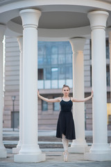 Fototapeta na wymiar Ballerina in a black dress is a beautiful pose. A beautiful young woman in a black bodysuit is dancing in an elegant classical dance on a background of columns.