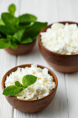fresh homemade cottage cheese in a wood bowl with mint leaves, on white background. top view