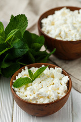fresh homemade cottage cheese in a wood bowl with mint leaves, on white background. top view