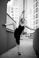 Ballerina in tutu makes an elegant pose. Beautiful young woman in black dress and pointe dancing over city background. Portrait of a gorgeous ballerina performing a dance outdoors. Black and white