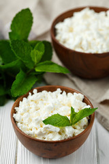 fresh homemade cottage cheese in a wood bowl with mint leaves, on white background. top view