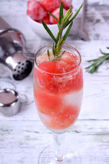 Sparkling cocktail with watermelon balls and rosemary in a champagne glass on white table
