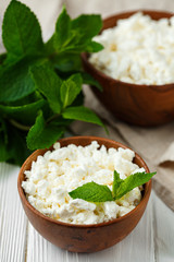 fresh homemade cottage cheese in a wood bowl with mint leaves, on white background. top view