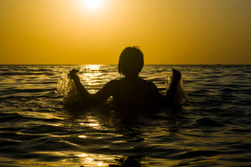 Fototapeta premium Girl swimming in the sea at sunset, splashes of transparency water, female black silhouette