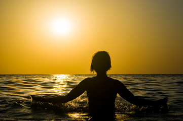 Fototapeta premium Girl swimming in the sea at sunset, splashes of transparency water, female black silhouette